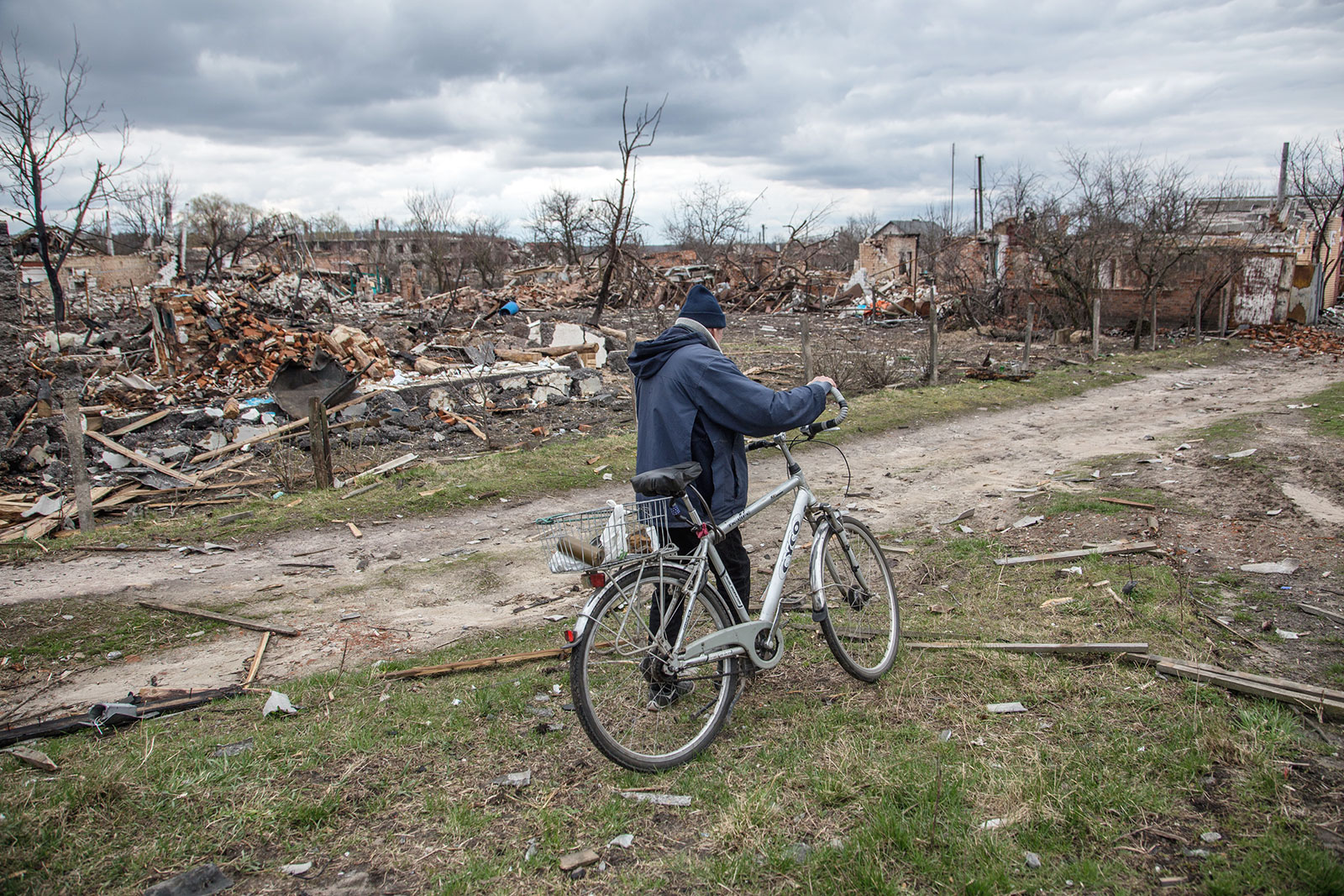 Person schiebt ein Fahrrad. Im Hintergrund Zerstörung durch den Krieg.