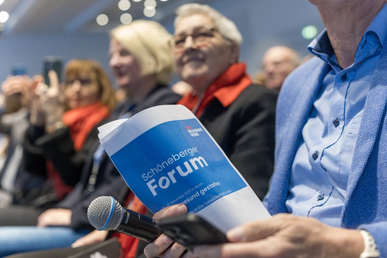 Gruppe reckt die Arme und steht vor einem blauen Rückwand mit dem Schriftzug Schöneberger Forum