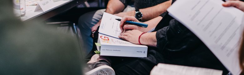 Hände halten ein Arbeitsgesetzbuch während eines Seminars, auf dem Tisch sind Notizen sichtbar.