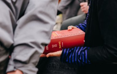 Hände halten ein BetrVG-Kommentarbuch, im Vordergrund eine Person mit grauem Hemd.