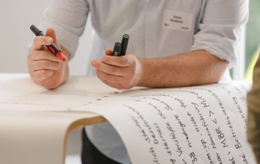 Hände schreiben auf Papier, mit Edding in der Hand