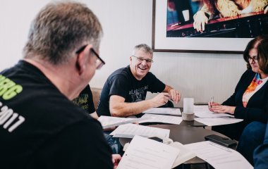 2 Männer und eine Frau sitzen am Tisch mit vielen Papieren und arbeiten zusammen